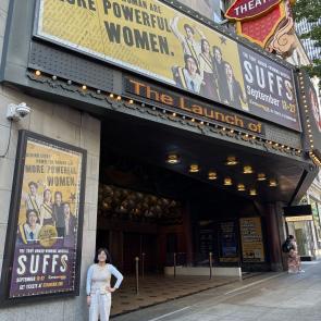 Sophie standing outside The 5th Avenue Theatre next to the SUFFS billboard.
